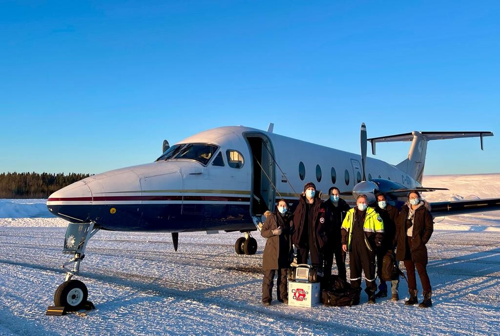 Group of six individuals in front of a small airplane in a snowy landscape
